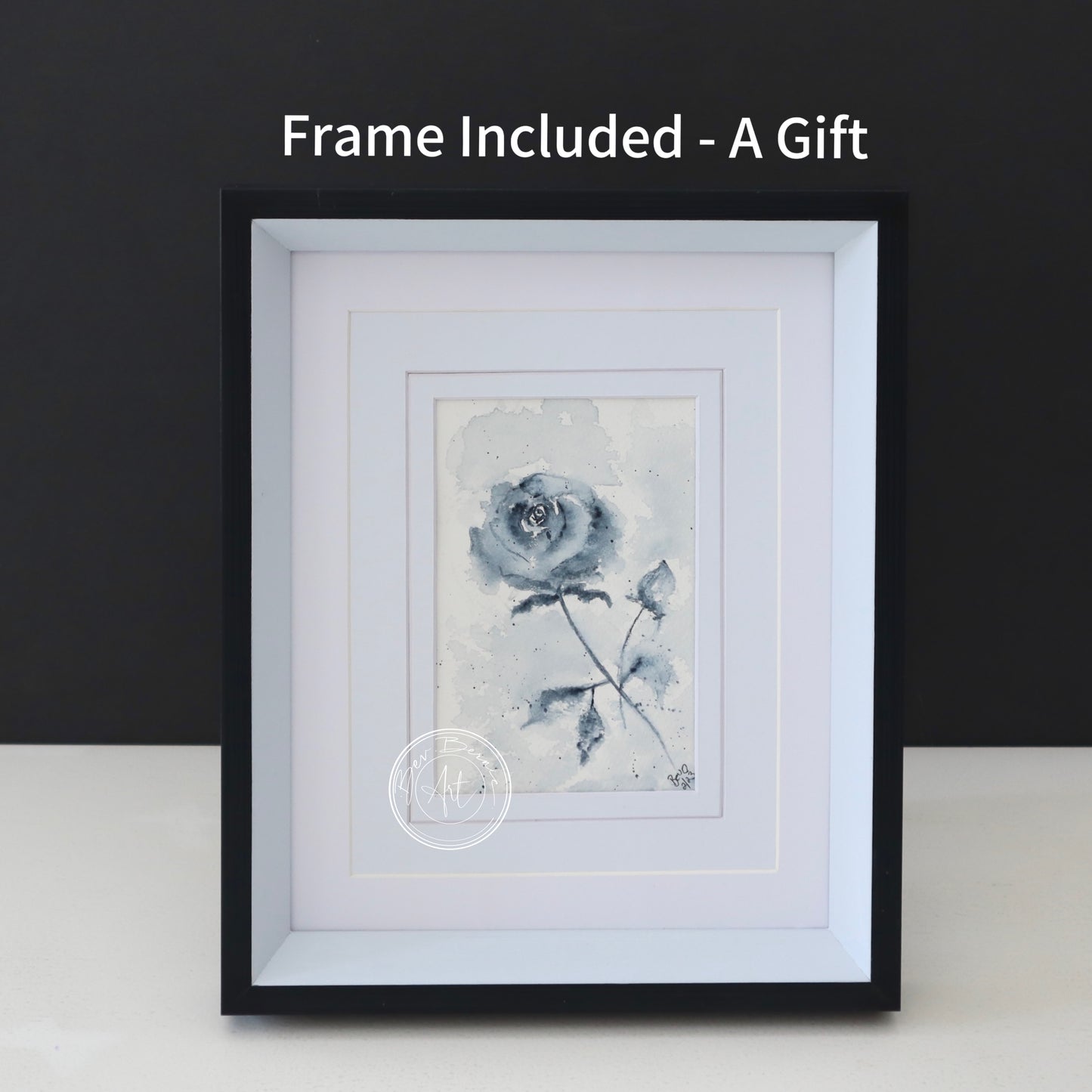 Watercolour painting of a single, stylised blue rose with a bud on a textured, off-white background, framed in a black frame with a white mat.