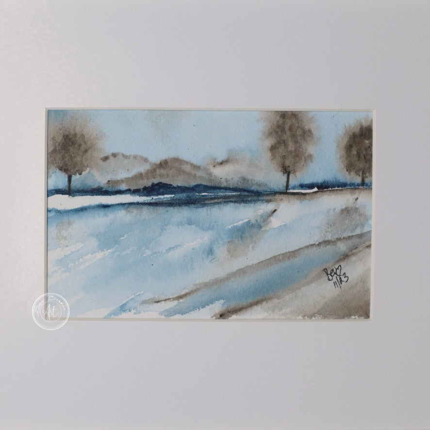 Three small square watercolor paintings in a row, depicting a minimalist winter landscape with blue, gray, and brown tones. The paintings are framed in a light wood frame with a wide white mat. Each painting shows a different aspect of the landscape, including water, reeds, and distant trees.